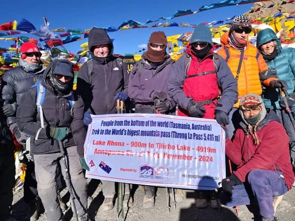 Trekkers At Thorong La Pass Summit Surrounded By Snow And Flags