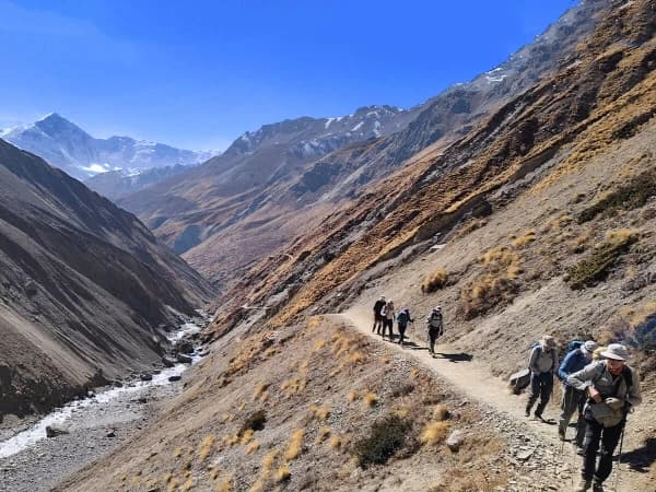 Trekkers Walking Along A Narrow Mountain Trail Dwarfed By The Surrounding Peaks
